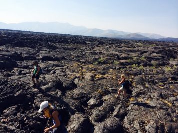 A contemporary color photograph of students crossing a rocky, cratered surface. A hazy mountain range is visible in the distance.